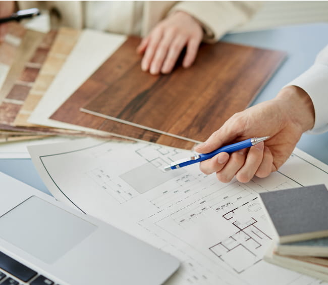 ノートパソコンの前で青いペンを使いながらプロジェクトに取り組む人物の画像